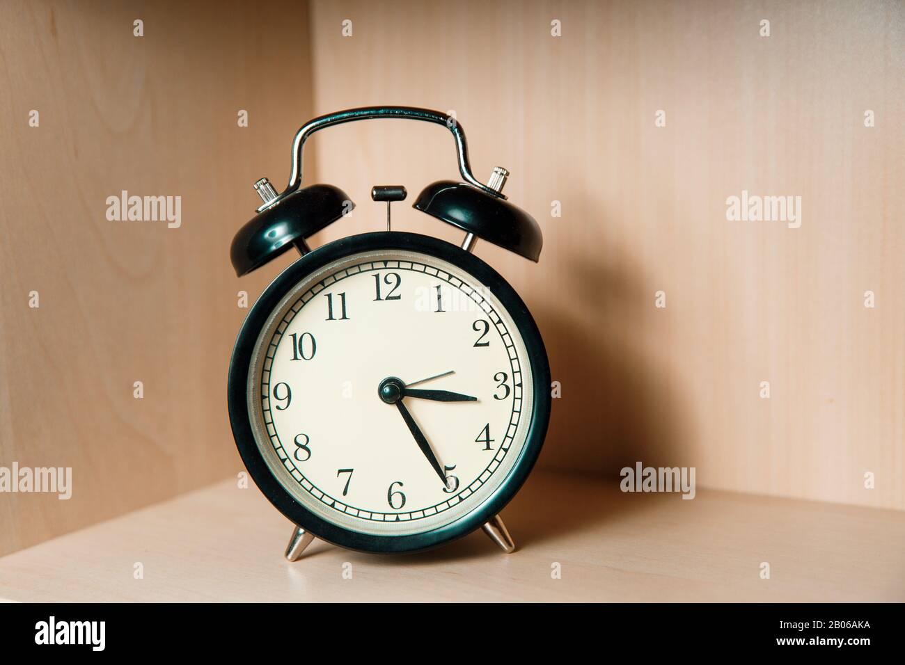Black retro alarm clock stands on a light wooden shelf. Classic alarm