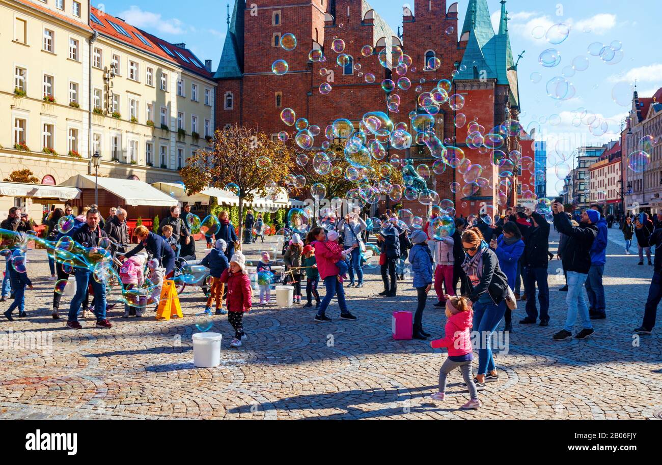 Children playing and having fun with soap bubbles at the old Market Square with the town hall in the background on a sunny day. Wroclaw, Poland. Stock Photo