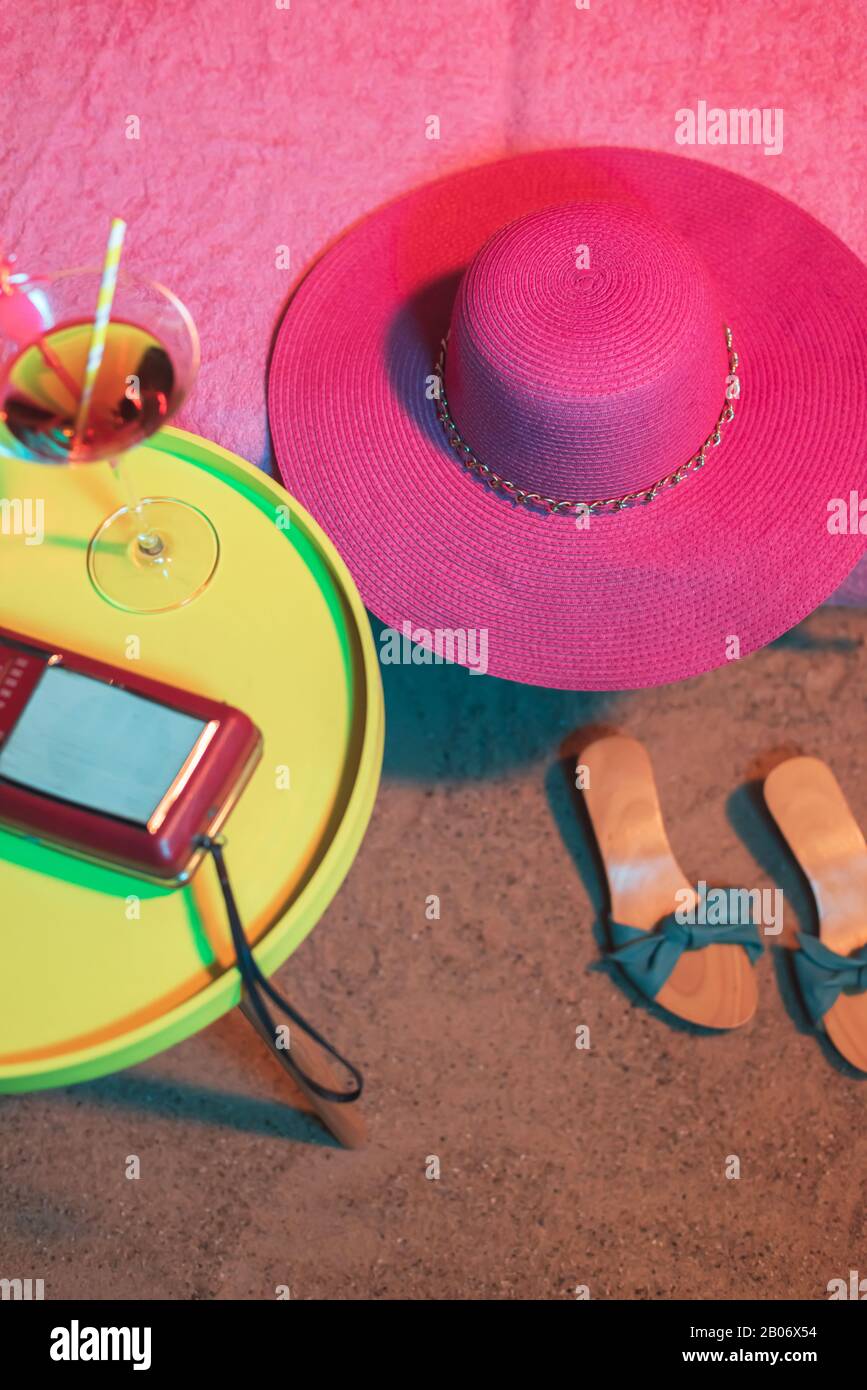 Pink beach hat on sunbed with vintage 1950s ladies shoes and yellow table  with cocktail and radio next to it Stock Photo - Alamy