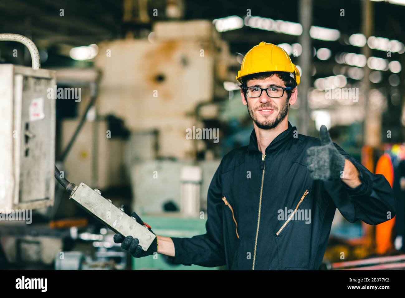 glasses nerdy worker show thumb up happy working in factory, industrial engineer man enjoy to work operate the machine. Stock Photo