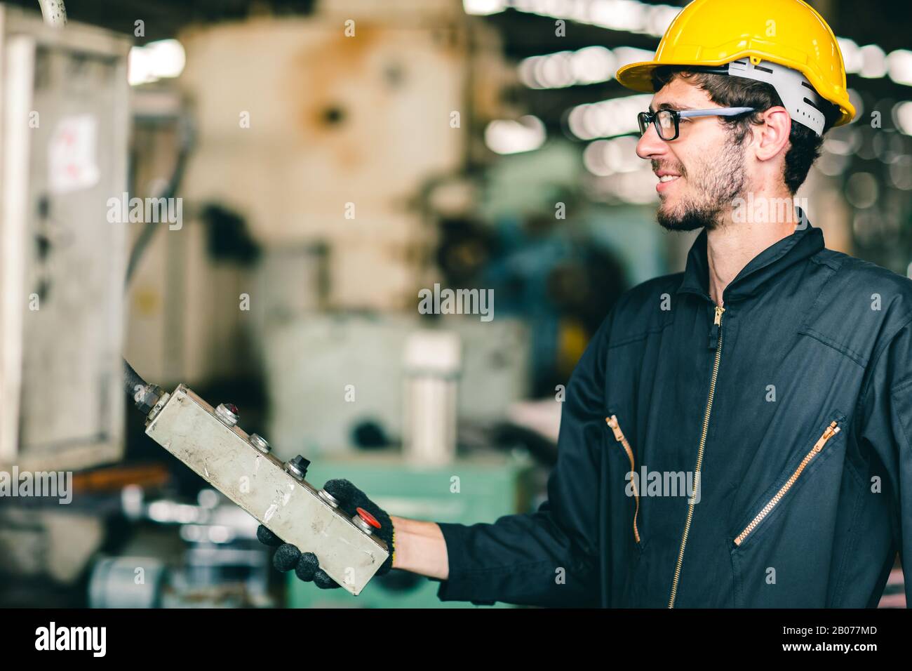 Labor worker engineer with safety suit and helmet happy smiling enjoy working operate heavy machine in industry factory. Stock Photo