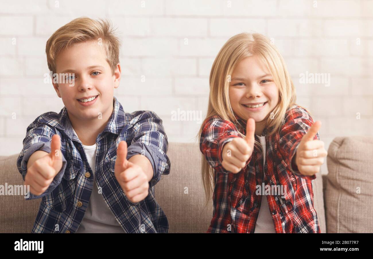 Brother And Sister Gesturing Thumbs-Up Sitting On Couch At Home Stock Photo