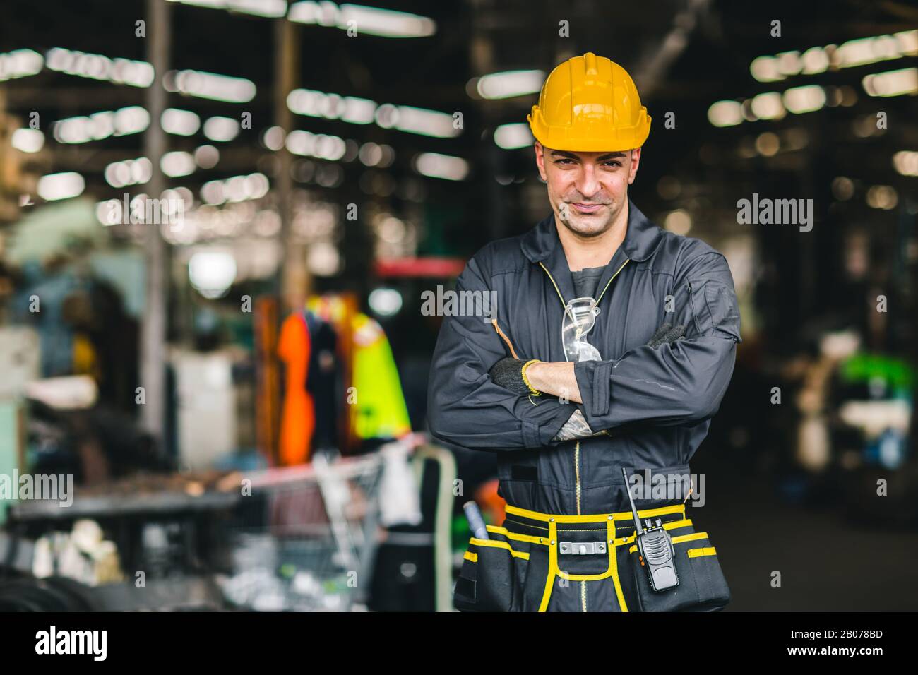 Happy worker, portrait handsome labor arms folded with safety suit tools belt and radio service man in factory. Stock Photo