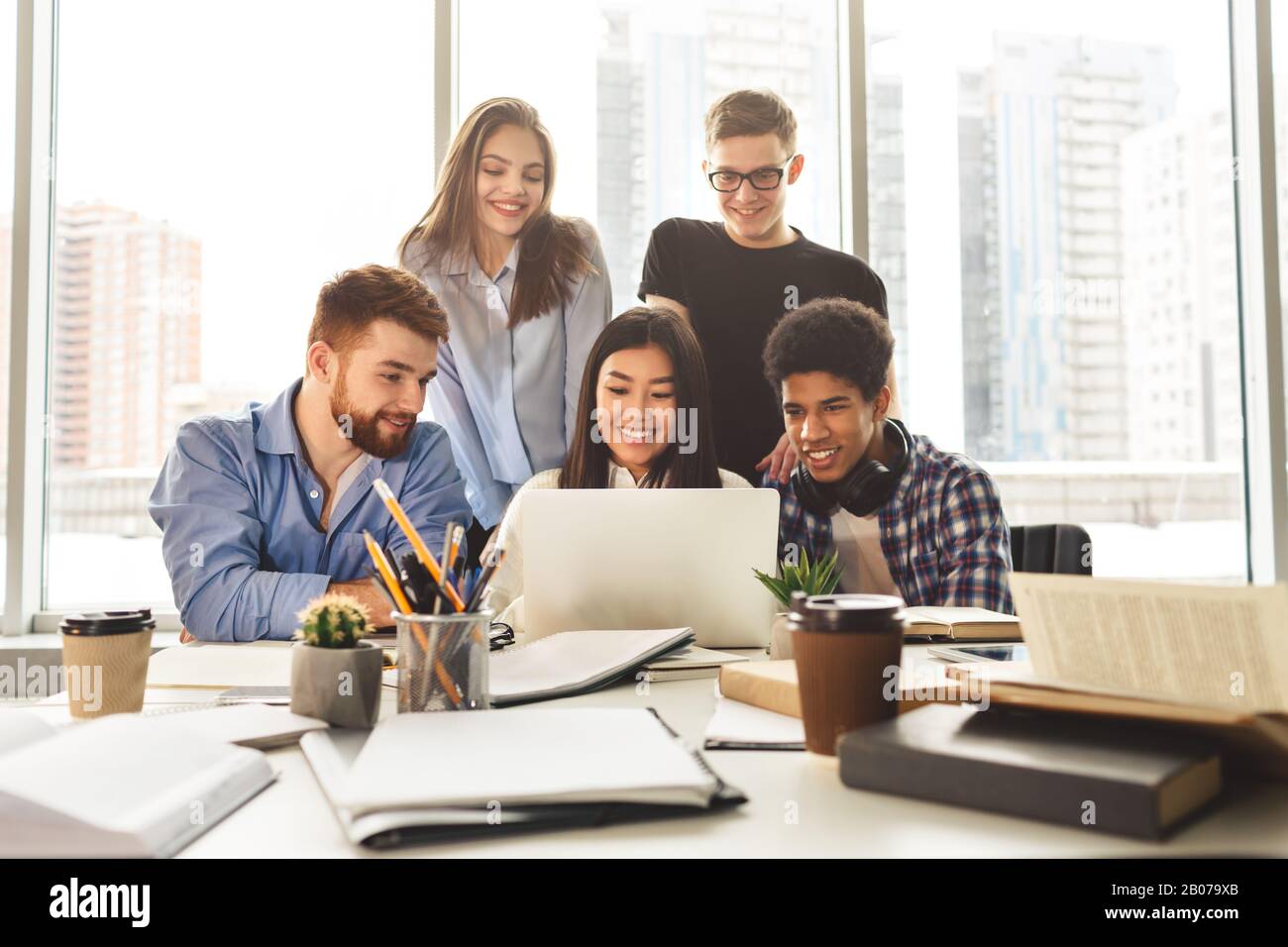 Multinational happy students gathering in library, using laptop Stock Photo