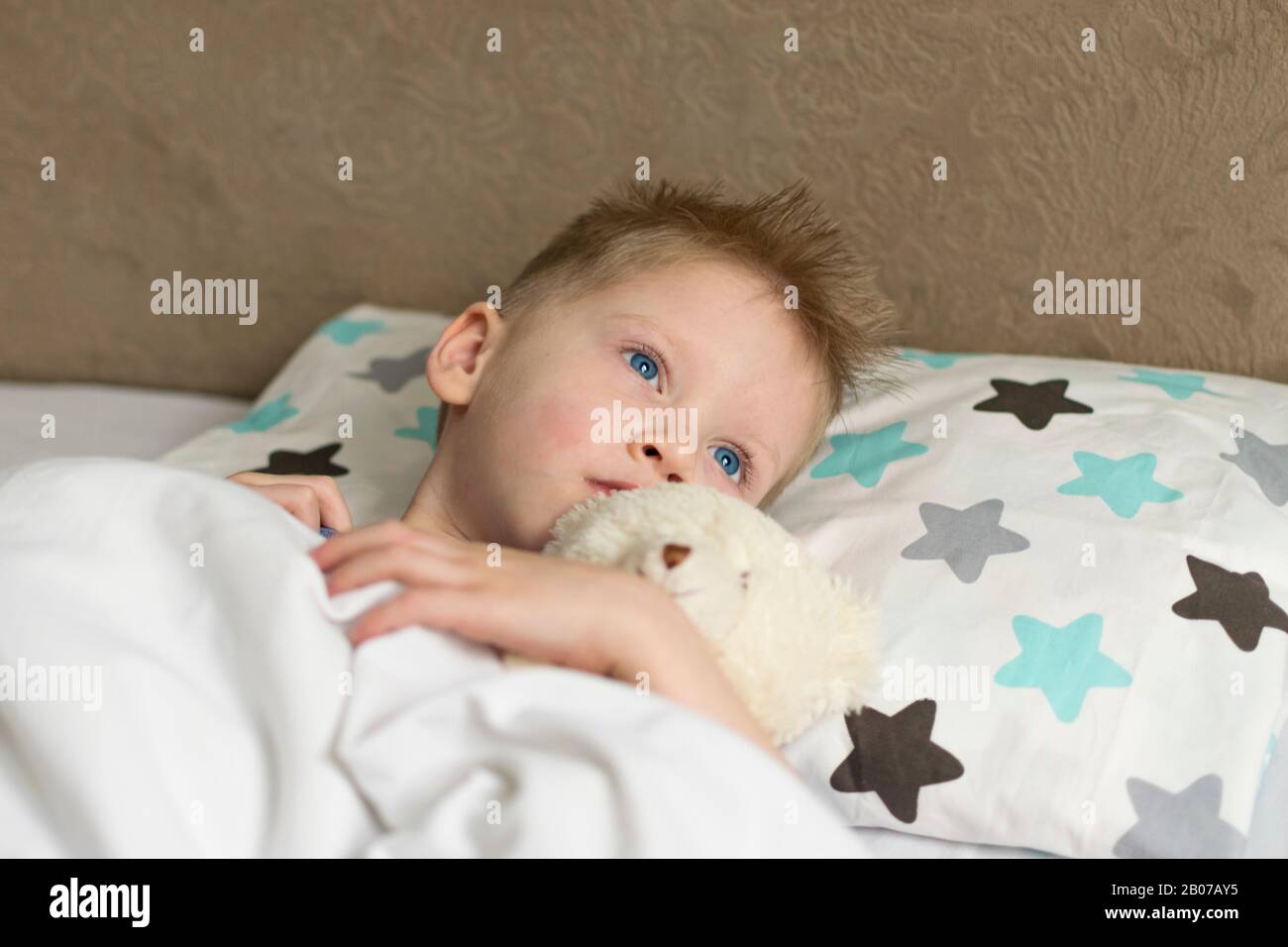 Sick sad child in temperature lies in bed with a toy bear. Flu colds disease virus bacterium Stock Photo