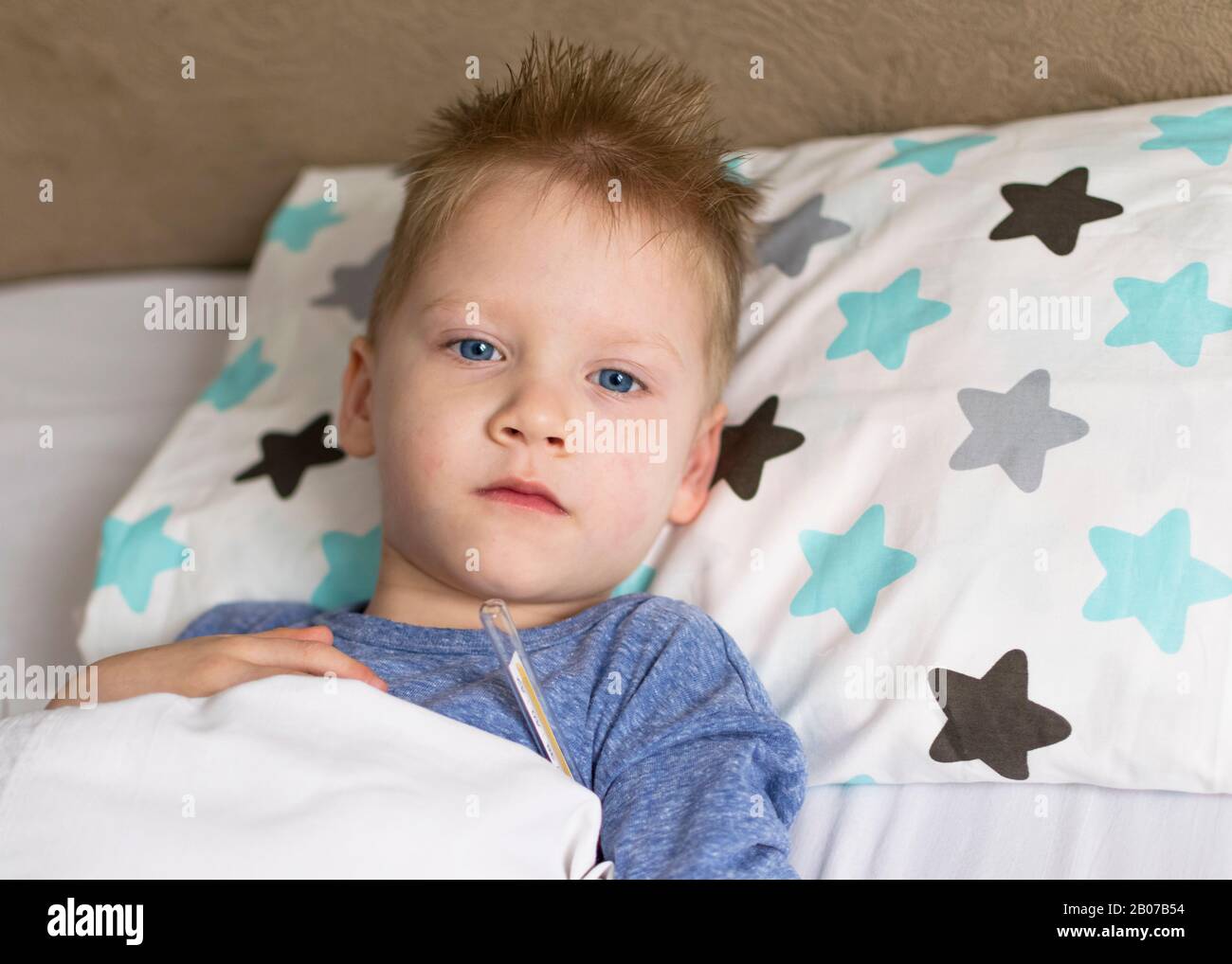 Sick sad child in temperature and headache lies in bed. Flu colds disease virus bacterium Stock Photo
