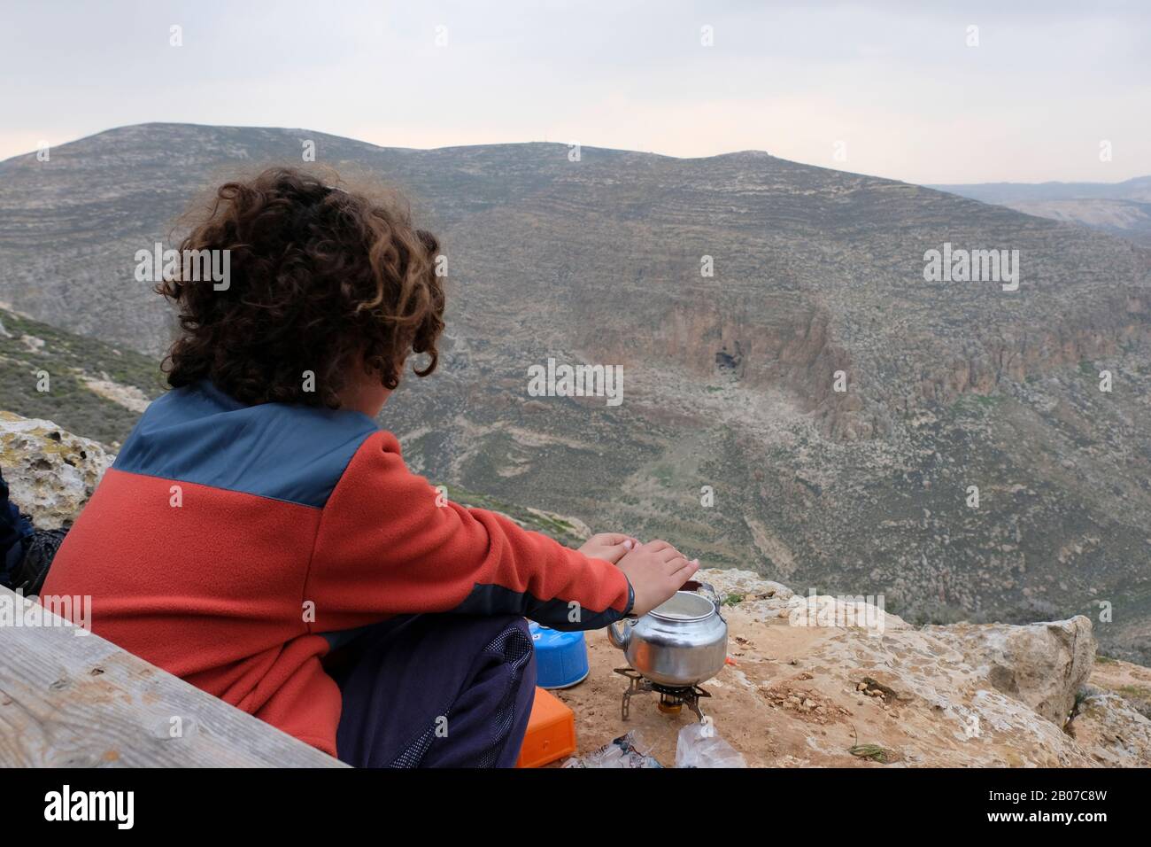 Young Jewish settler heating his hands over a pot of water boiling on a gas burner at the canyon of Nahal Arugot river in Gush Etzion a cluster of Jewish settlements located in the Judaean Mountains in the West Bank Israel Stock Photo