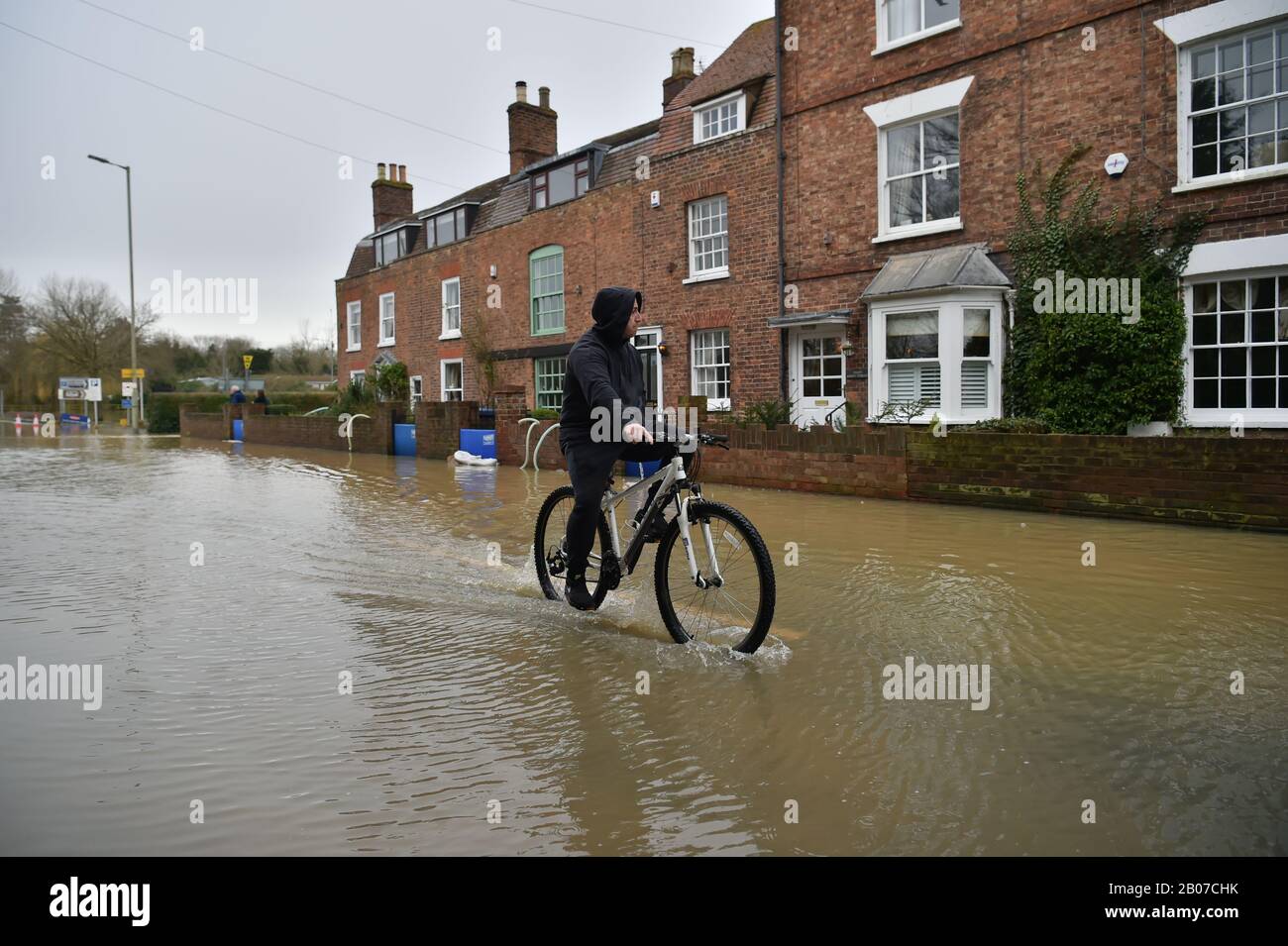 A man rides a bike through flood water, as pumps and flood barriers help to keep the water from flooding homes in Gloucester Road in Tewkesbury, Gloucestershire, following the aftermath of Storm Dennis. Stock Photo