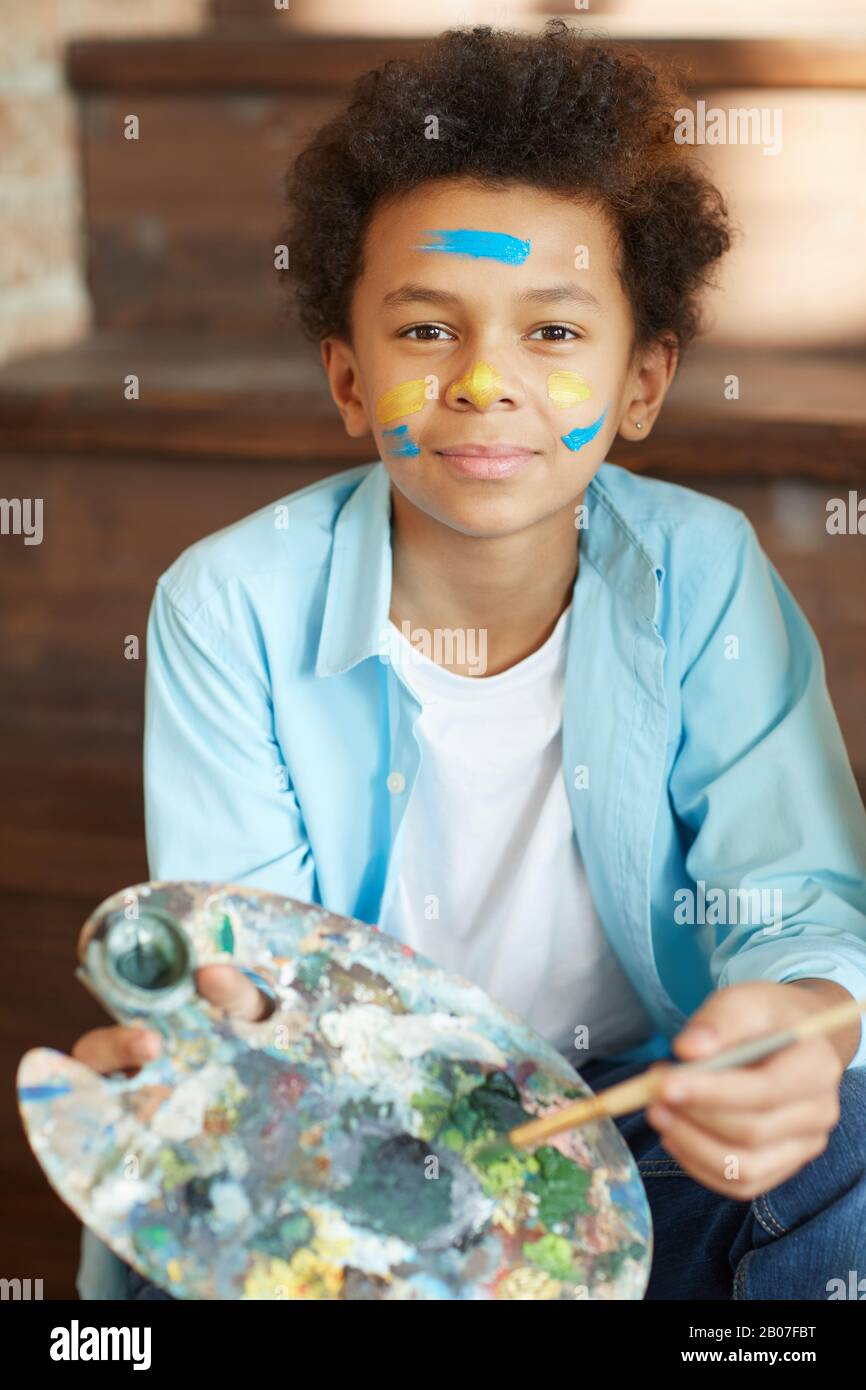 Portrait of African young boy holding palette with paints and looking at camera he painting at studio Stock Photo