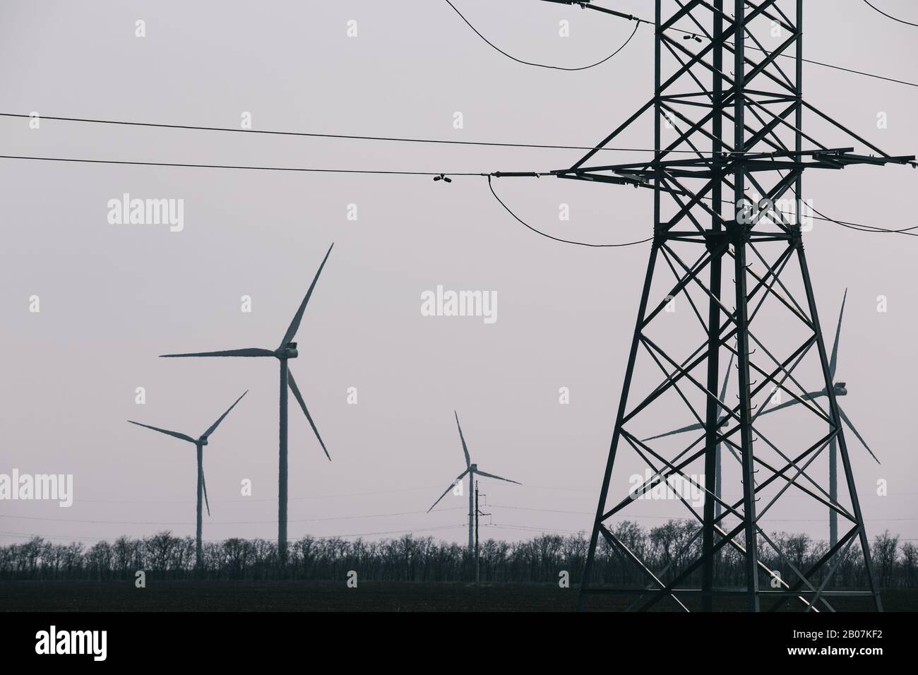 Electricity transmission pylon and wind turbine of gray sky on background Stock Photo