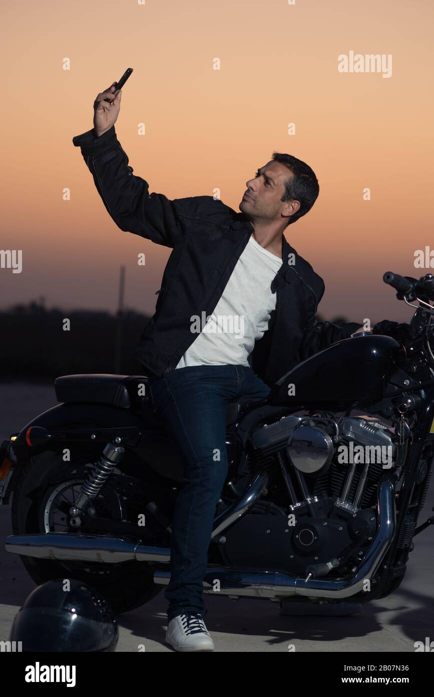 Male biker on his motorcycle with a taking a selfie smartphone. Stock Photo