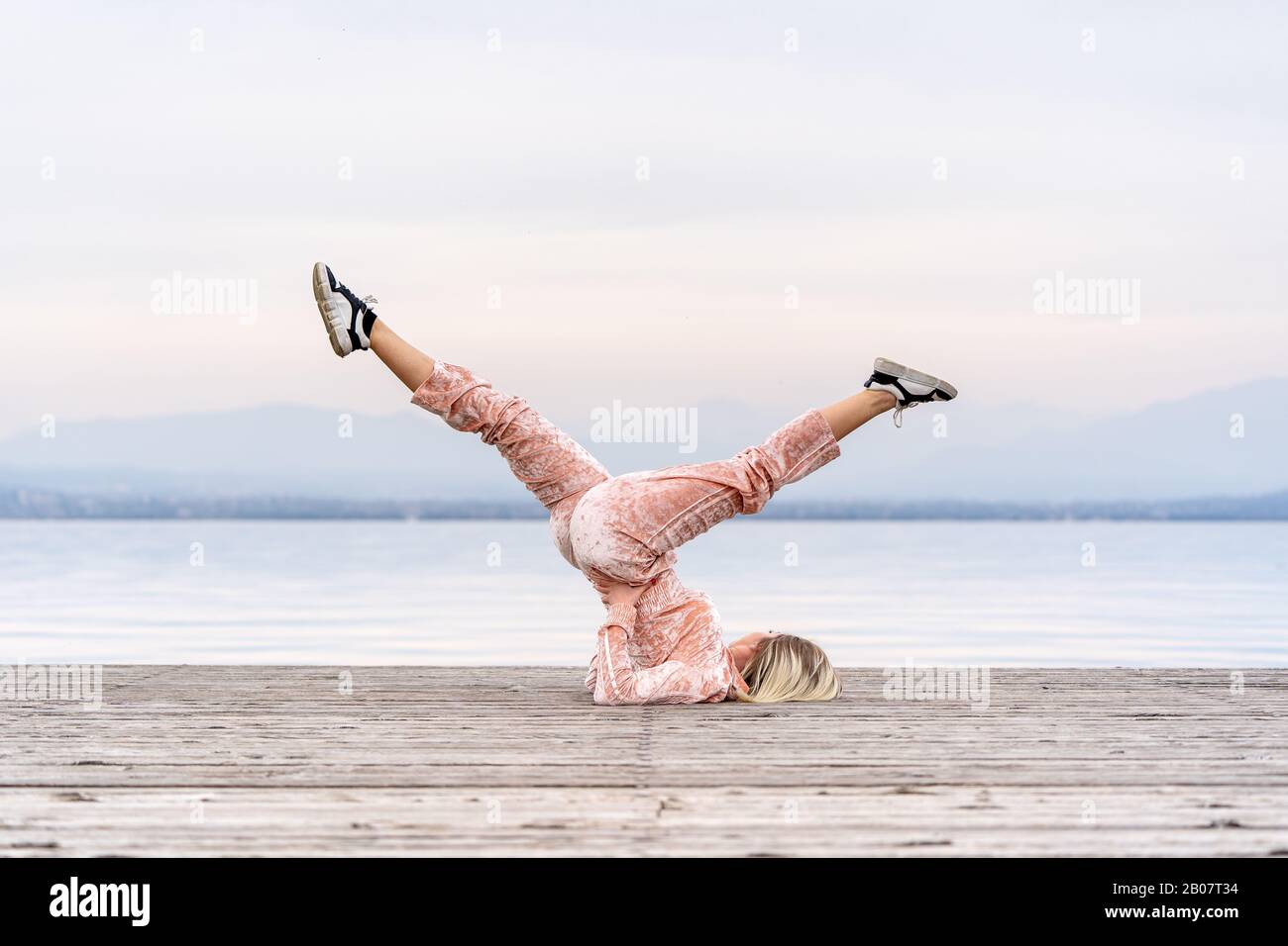 A beautiful woman performs the exercises lifting her legs to the top, lake, pier, Fitness. Sport. Yoga. Stock Photo