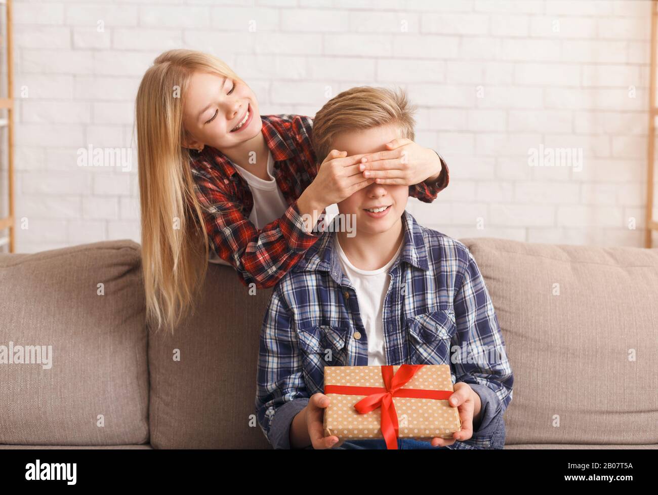 Girl Covering Brother's Eyes Giving Him Birthday Gift Indoor Stock Photo