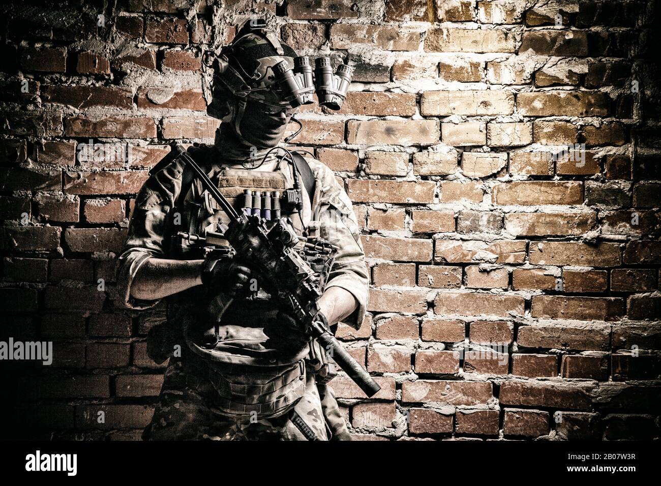 Special operations forces soldier, counter terrorism assault team fighter with night vision device on helmet and service rifle, low key indoor shot brick wall Stock Photo