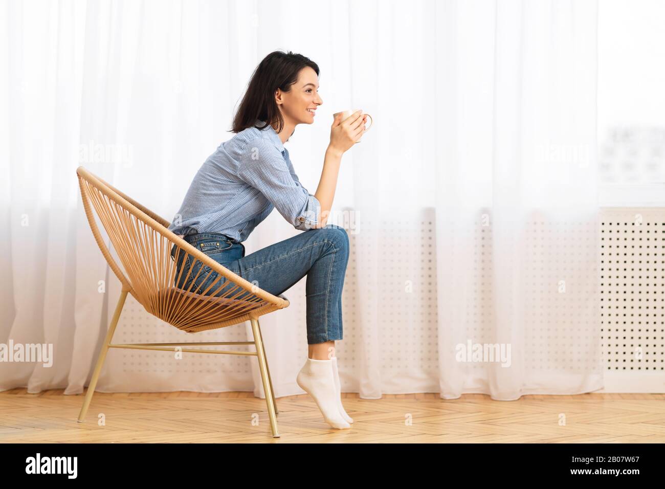 European Girl Sitting In Modern Chair Enjoying Morning Coffee Stock Photo