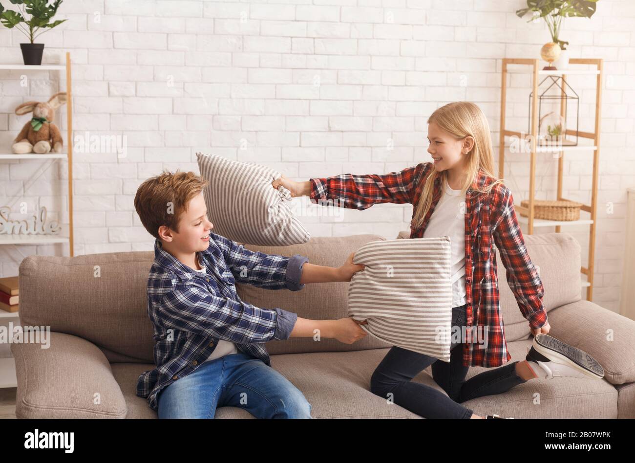 Sibling Having Fun Fighting With Pillows On Couch Indoor Stock Photo