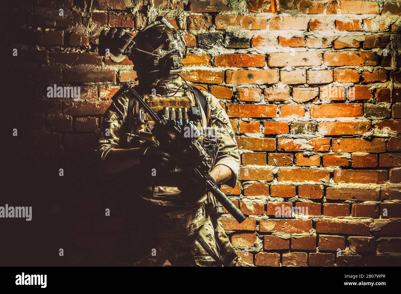 Special operations forces soldier, counter terrorism assault team fighter with night vision device on helmet and service rifle, low key indoor shot brick wall Stock Photo
