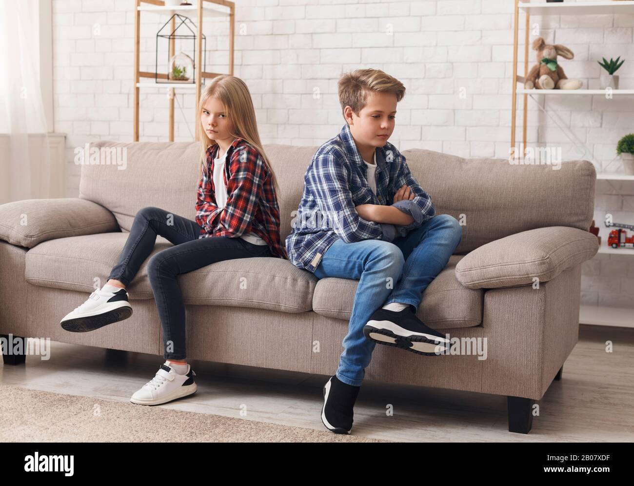 Offended Brother And Sister Sitting Back-To-Back On Sofa At Home Stock Photo