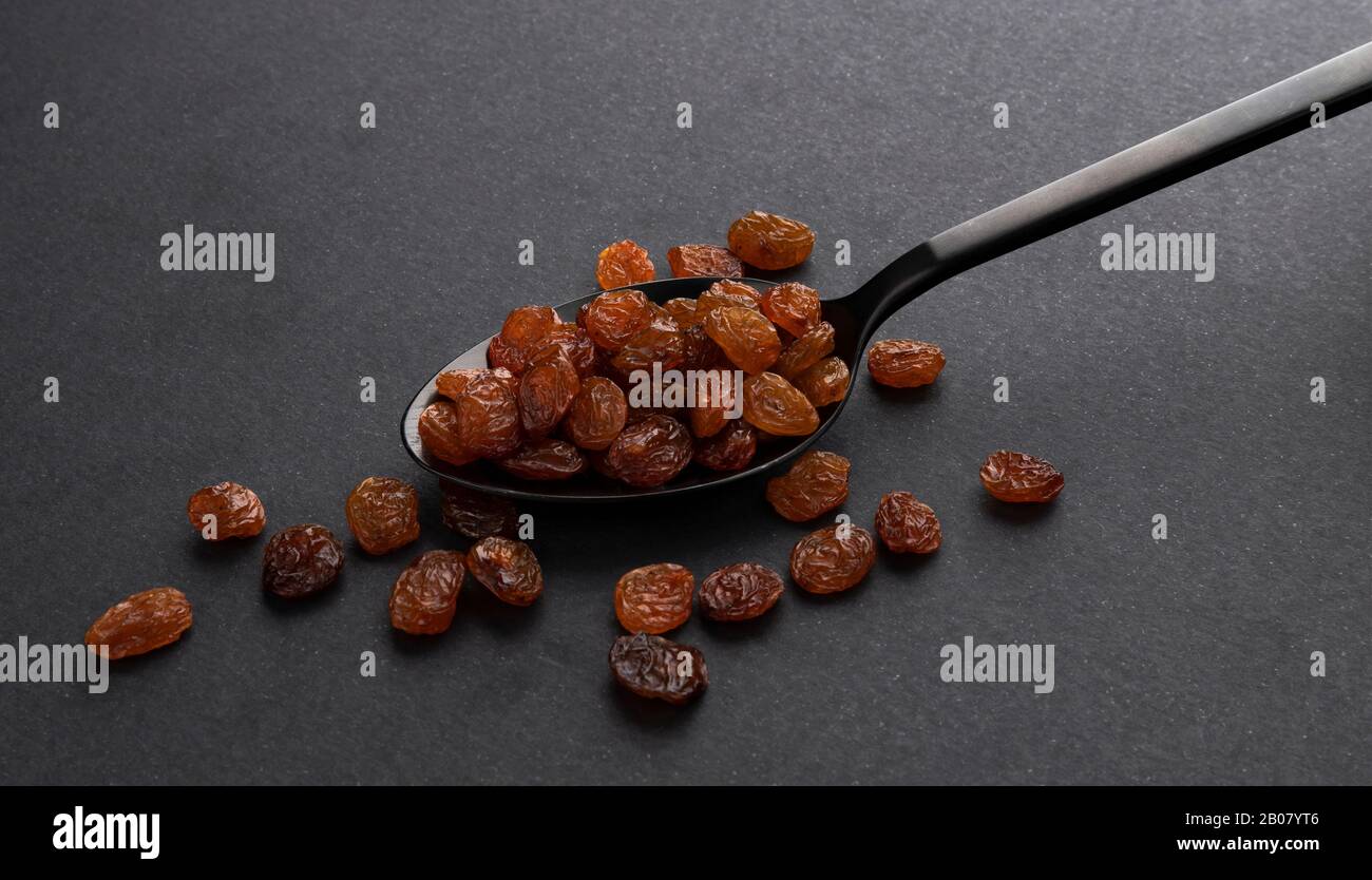 Pile of raisins in spoon on black background Stock Photo