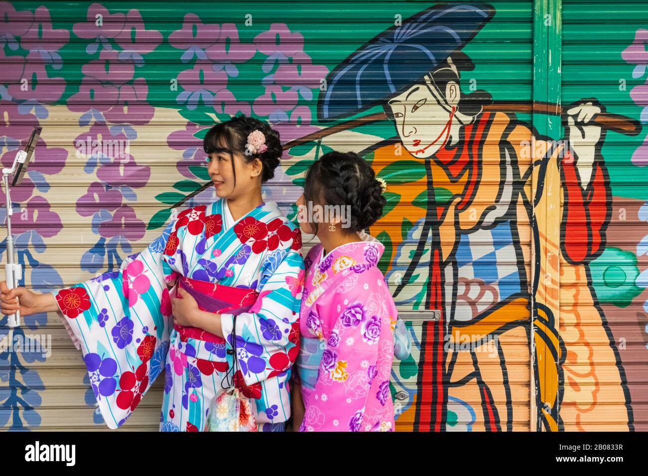 Japan, Honshu, Tokyo, Asakusa, Two Women in Kimono Taking Selfie Photos in front of Colourful Store Shutter Painting Stock Photo