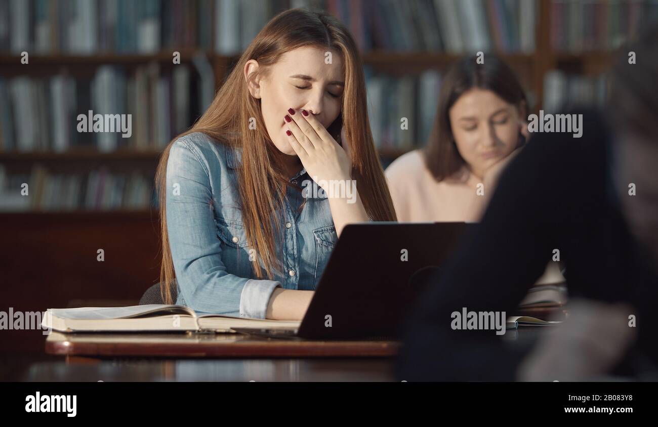 Yawning girl working laptop, library Stock Photo