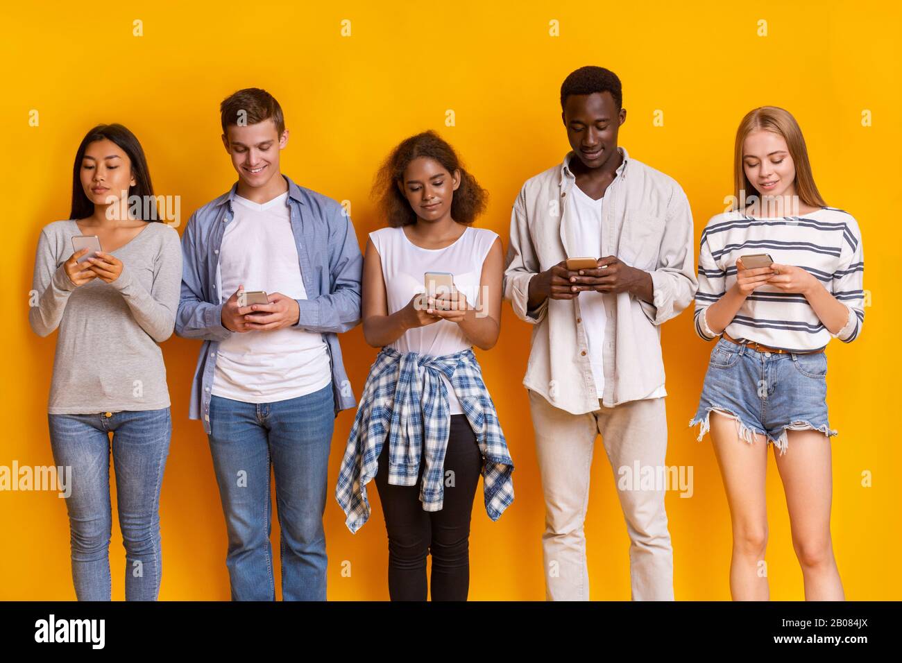 Young friends staying in row, using mobile phones Stock Photo