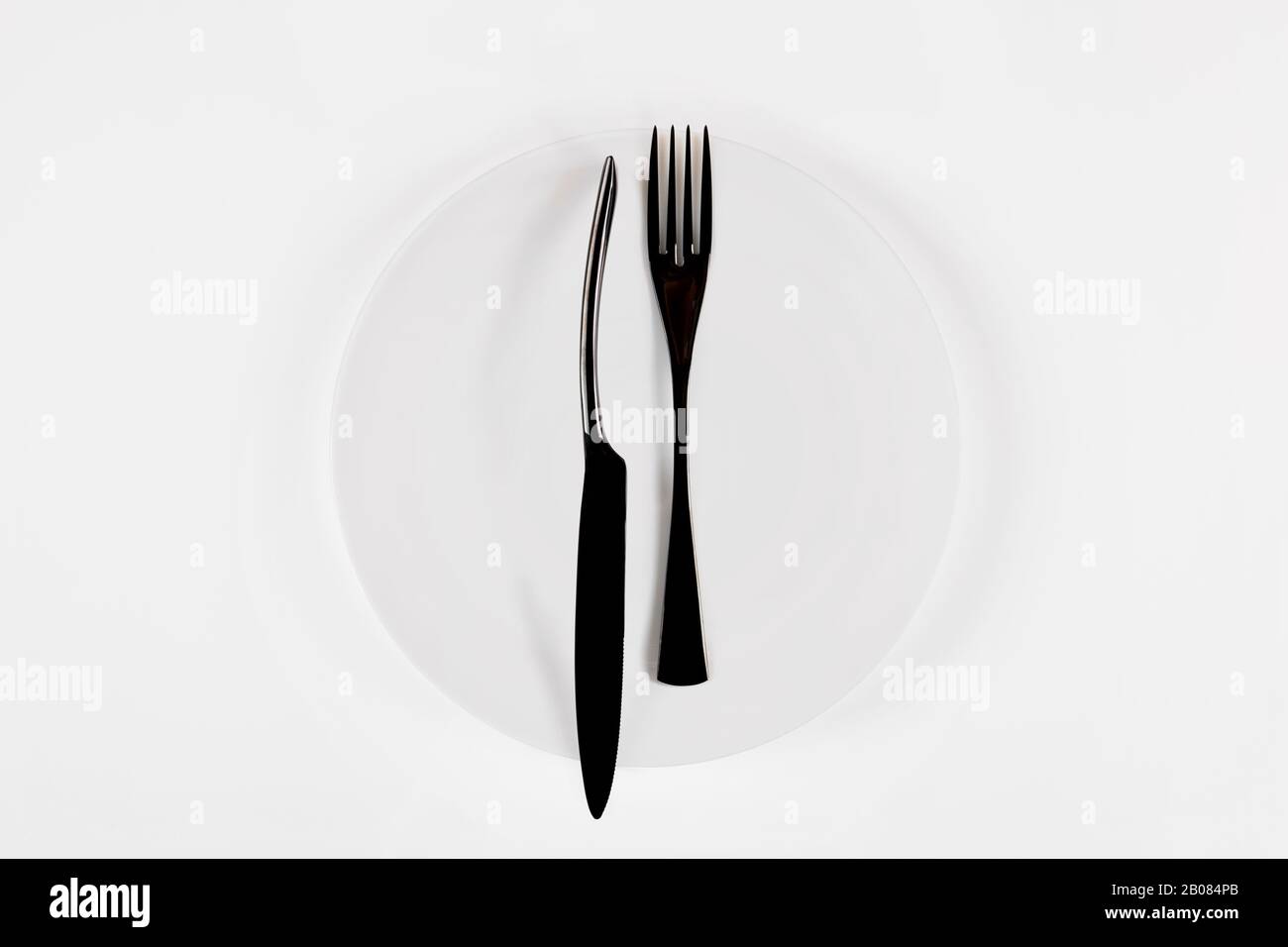 Cutlery language, dining etiquette. White ceramic round plate with knife anf fork isolated on white, top view. Stock Photo