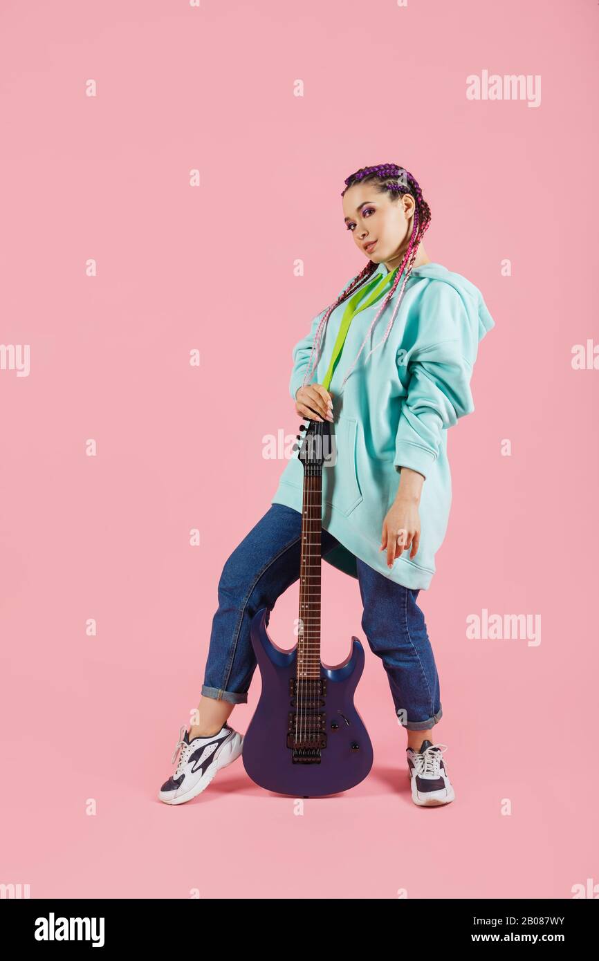 Young guitarist woman in oversize clothes with electric guitar isolated on pink background Stock Photo