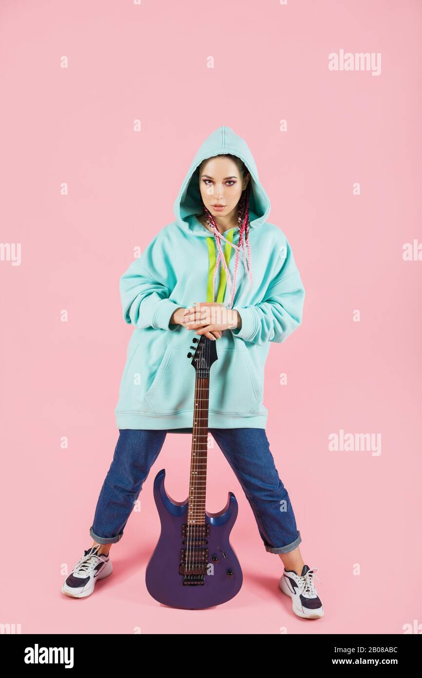 Young guitarist woman in oversize clothes with electric guitar amp isolated on pink background Stock Photo