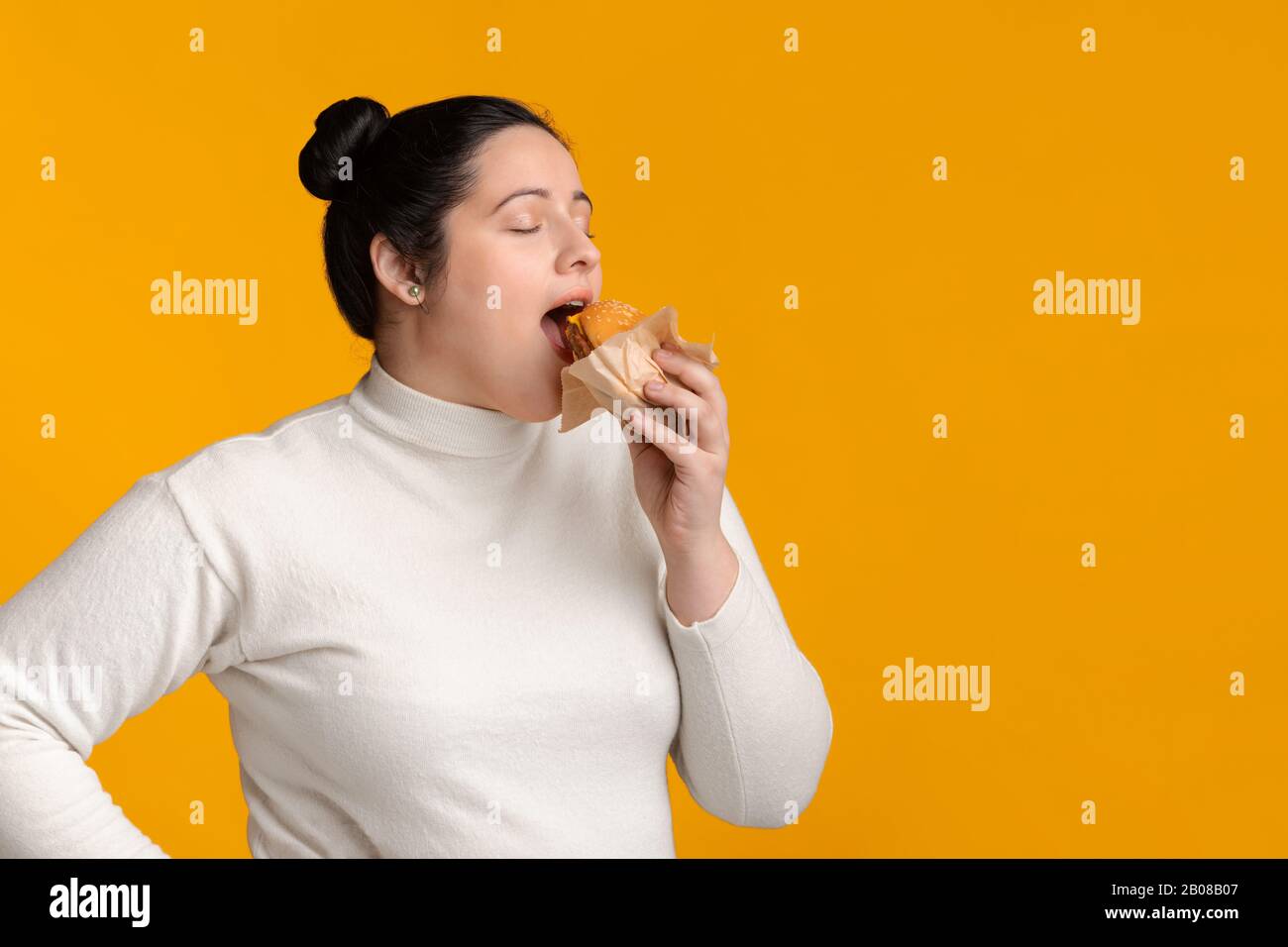 Young Plump Woman Eating Tasty Hamburger With Closed Eyes Stock Photo