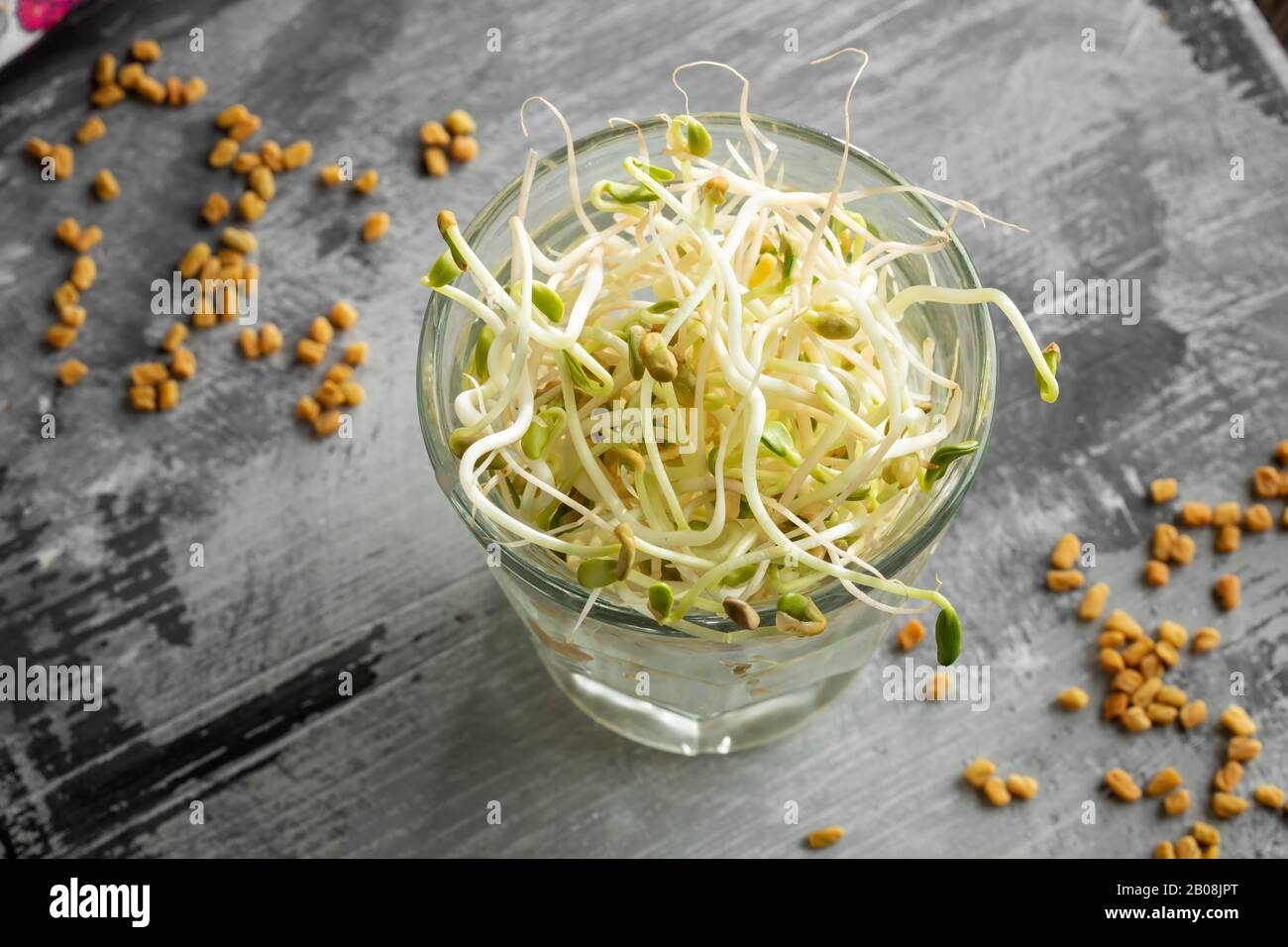 Fresh fenugreek sprouts in a glass, with dry seeds in the background Stock Photo