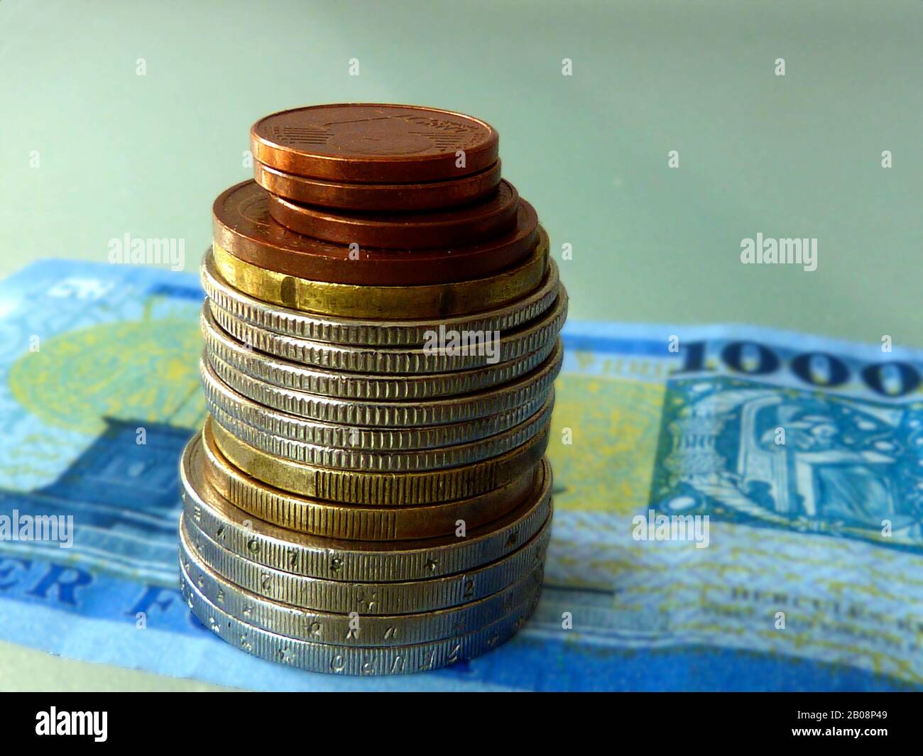stacking coins concept. various nickel chrome and copper various coins stacked in a small pile on top of blue paper bill. saving theme Stock Photo