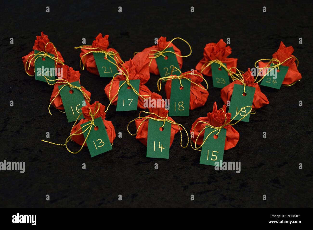 Twenty four little presents wrapped in red, green tags golden numbers from 1 to 24 on black as self made advent calendar - 13th of December Stock Photo