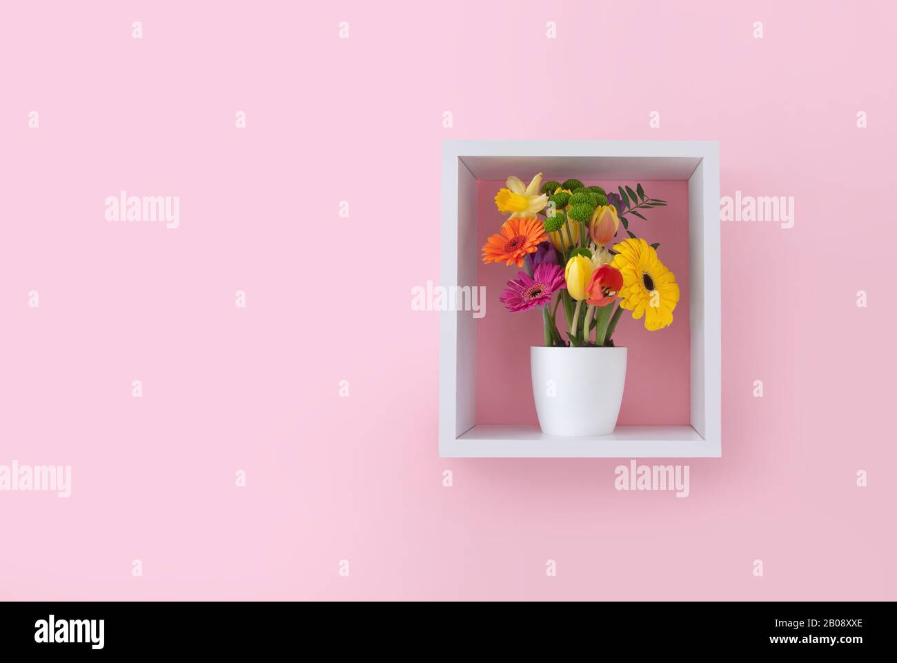 Spring flowers in a cube shelf display unit against pink wallpaper ...