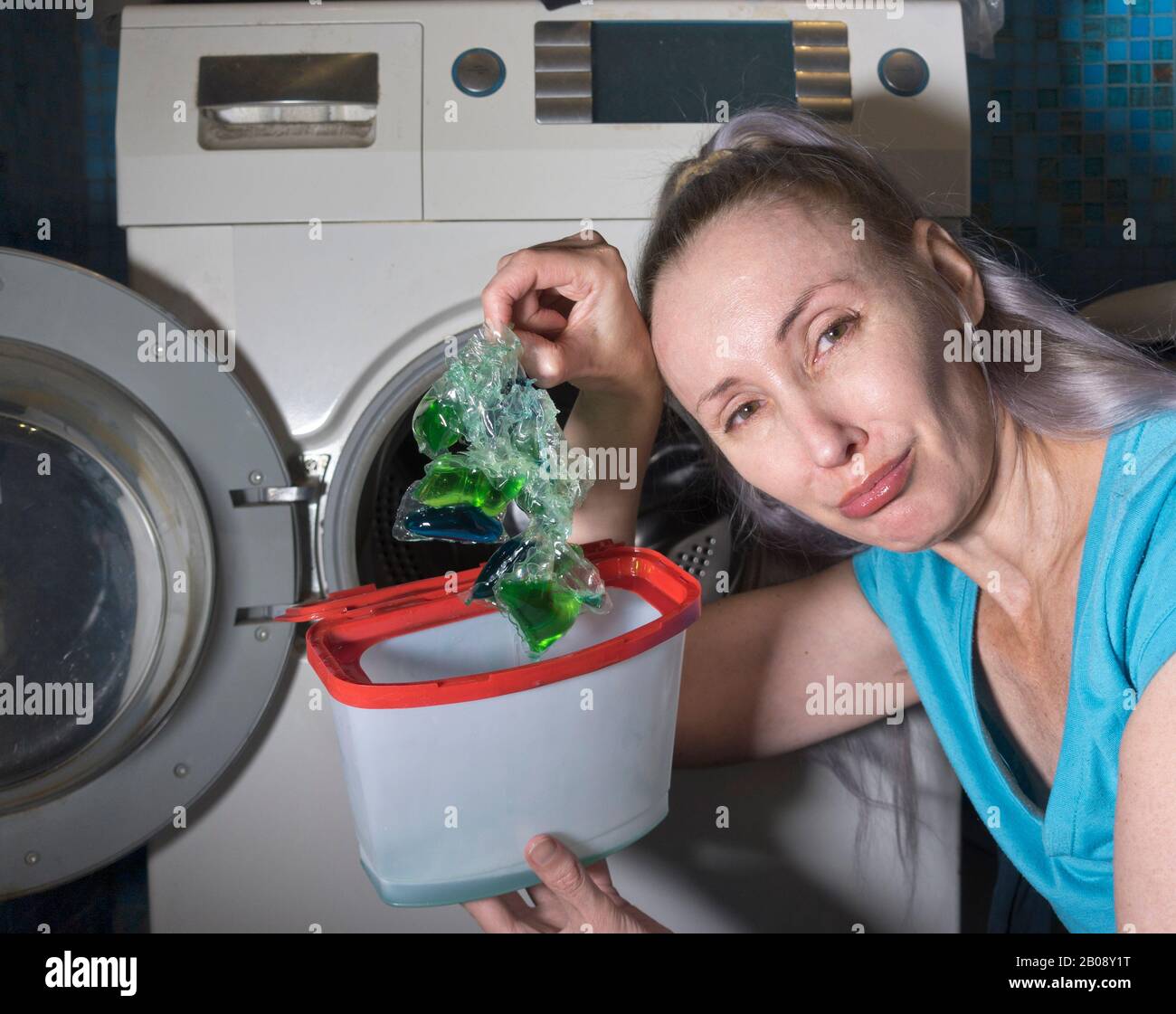 woman in the bathroom, next to the washing machine, takes out the defective washing gel stuck into one lump from the packaging and crying, photo from Stock Photo