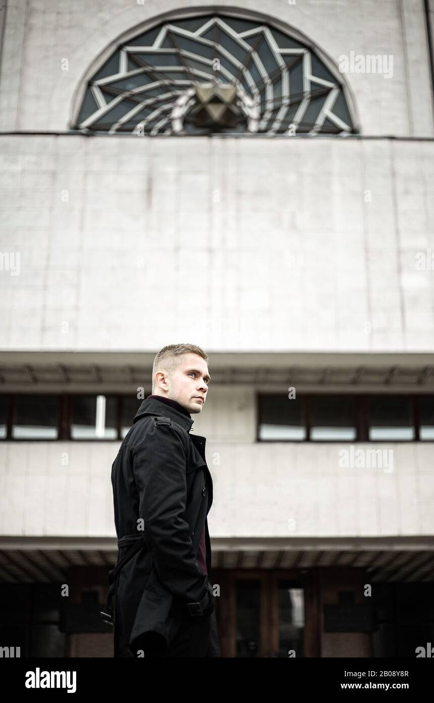 Stylish man in black trench coat and polo neck on modernist building background Stock Photo
