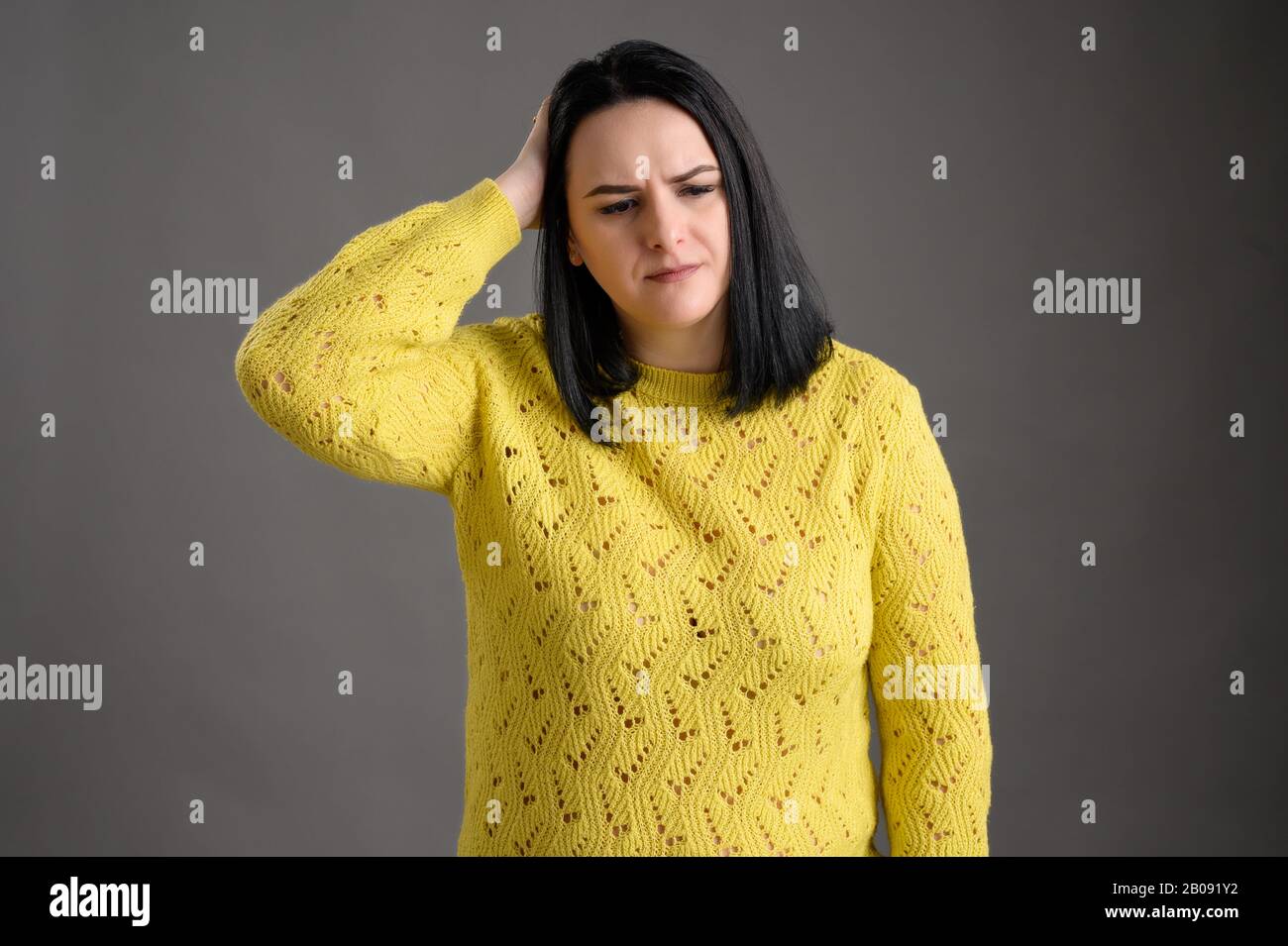 Young woman with black hair dressed casually in a yellow sweater has headaches posing an isolated grey background Stock Photo