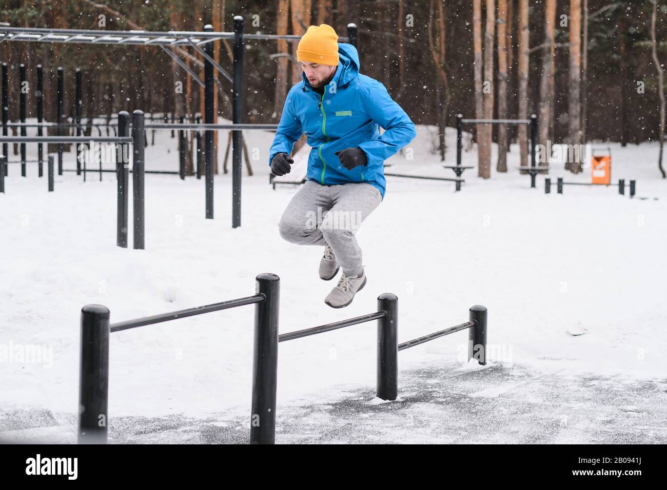 Young man in jacket jumping through horizontal bars of different heights while training in winter outdoors Stock Photo