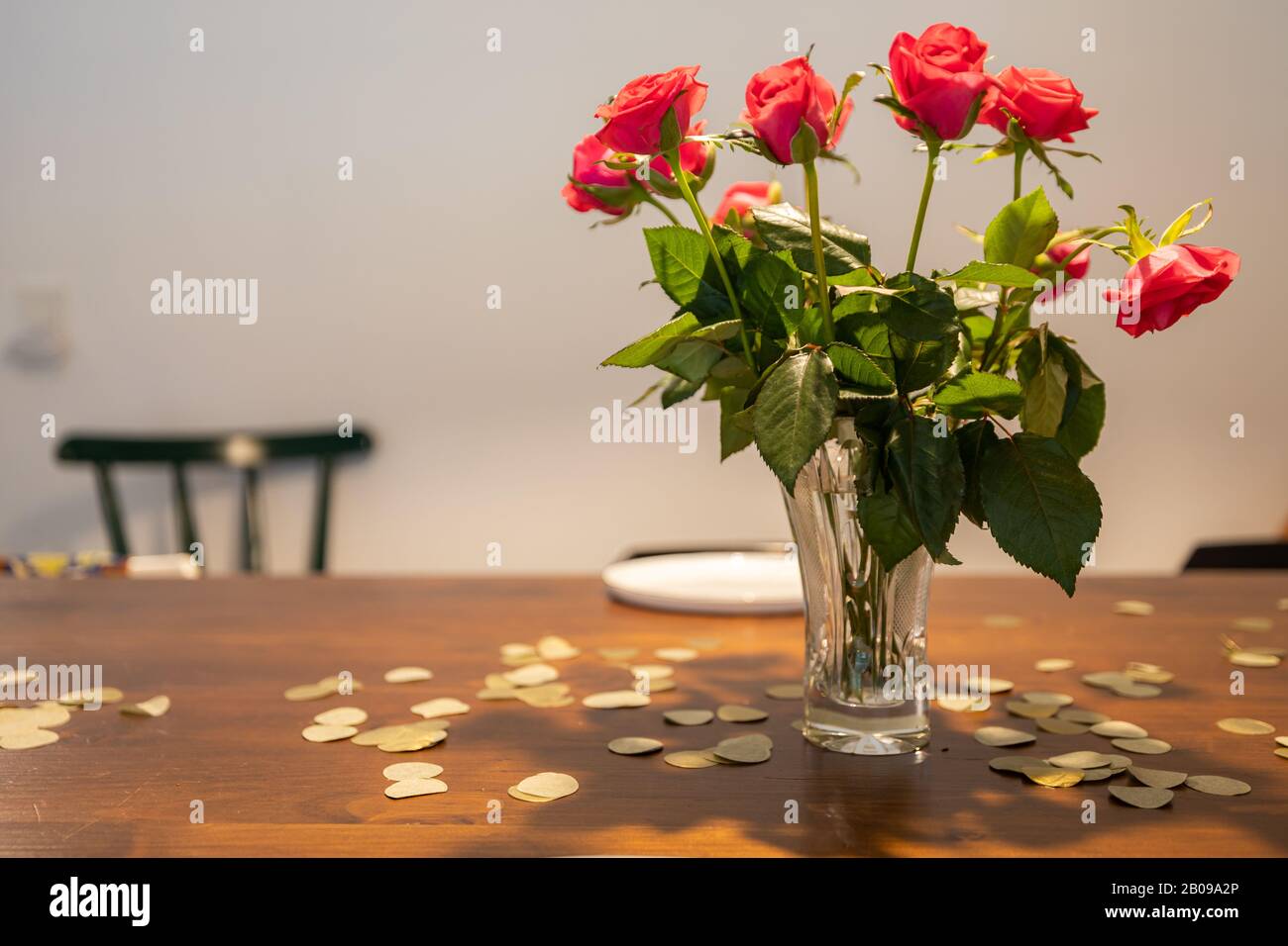 Vase with red roses on a table with gold confetti. Stock Photo