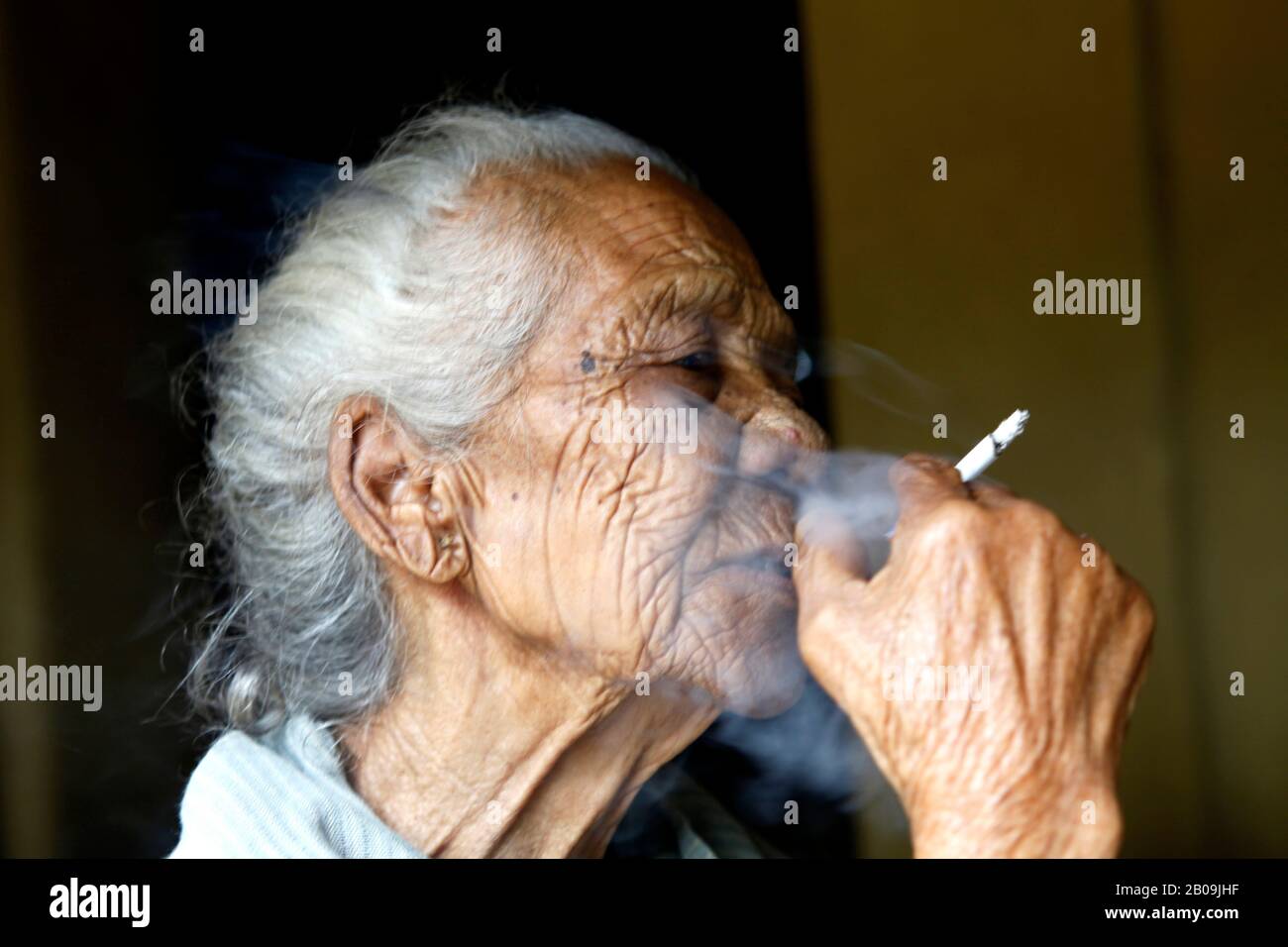 An elderly woman from the Garo community smokes a cigarette. Haluaghat,  Mymensingh, Bangladesh. September 26, 2010 Stock Photo