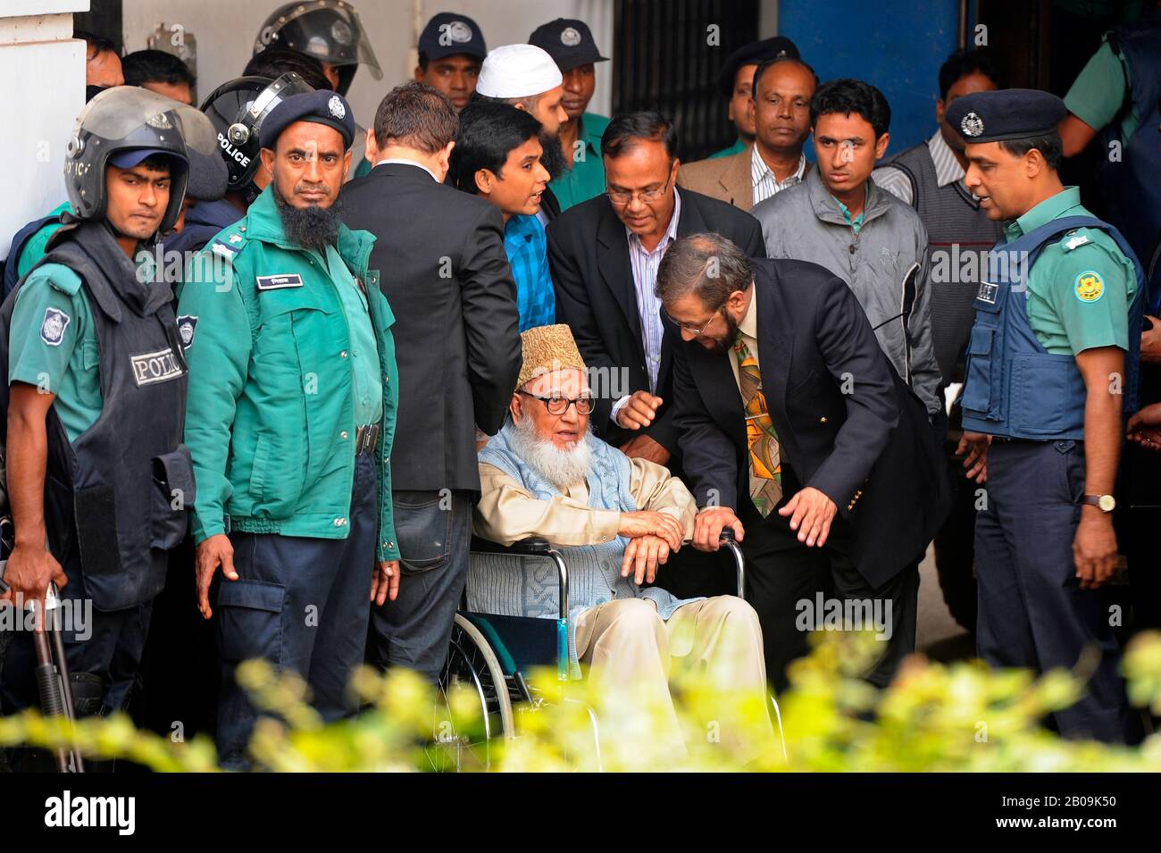 Police officers help former Jamaat-e-Islami chief Ghulam Azam, in a wheelchair, to get on board a prison van as he exits the Bangladesh International Crimes Tribunal. His bail plea was rejected by a special tribunal that sentenced him with imprisonment pending trial on charges committed against humanity during the liberation war of 1971. Dhaka, Bangladesh. January 11, 2012. Stock Photo