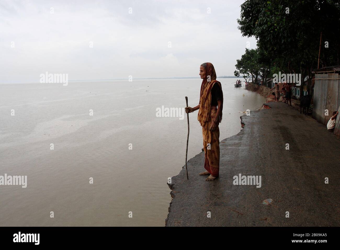 An elderly woman looks out from the remains of a road most of which has been eroded away in the Jamuna river in Sirajganj. Nearly 0.7 million people of the northern district have been affected by the severe flood of 2007. Sirajganj, Bangladesh. August 1, 2007. Stock Photo