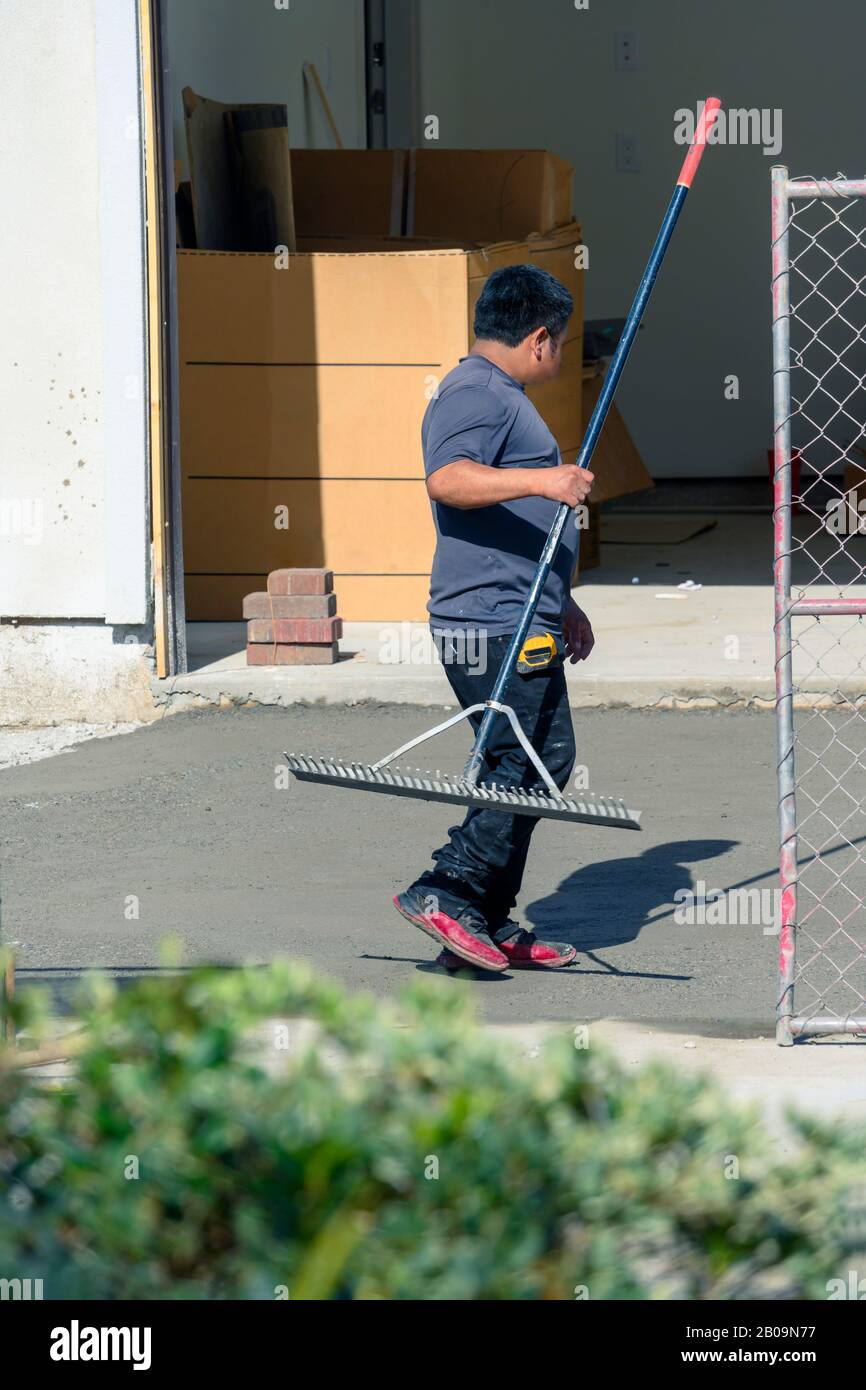 Construction worker raking freshly poured concrete mix on driveway in