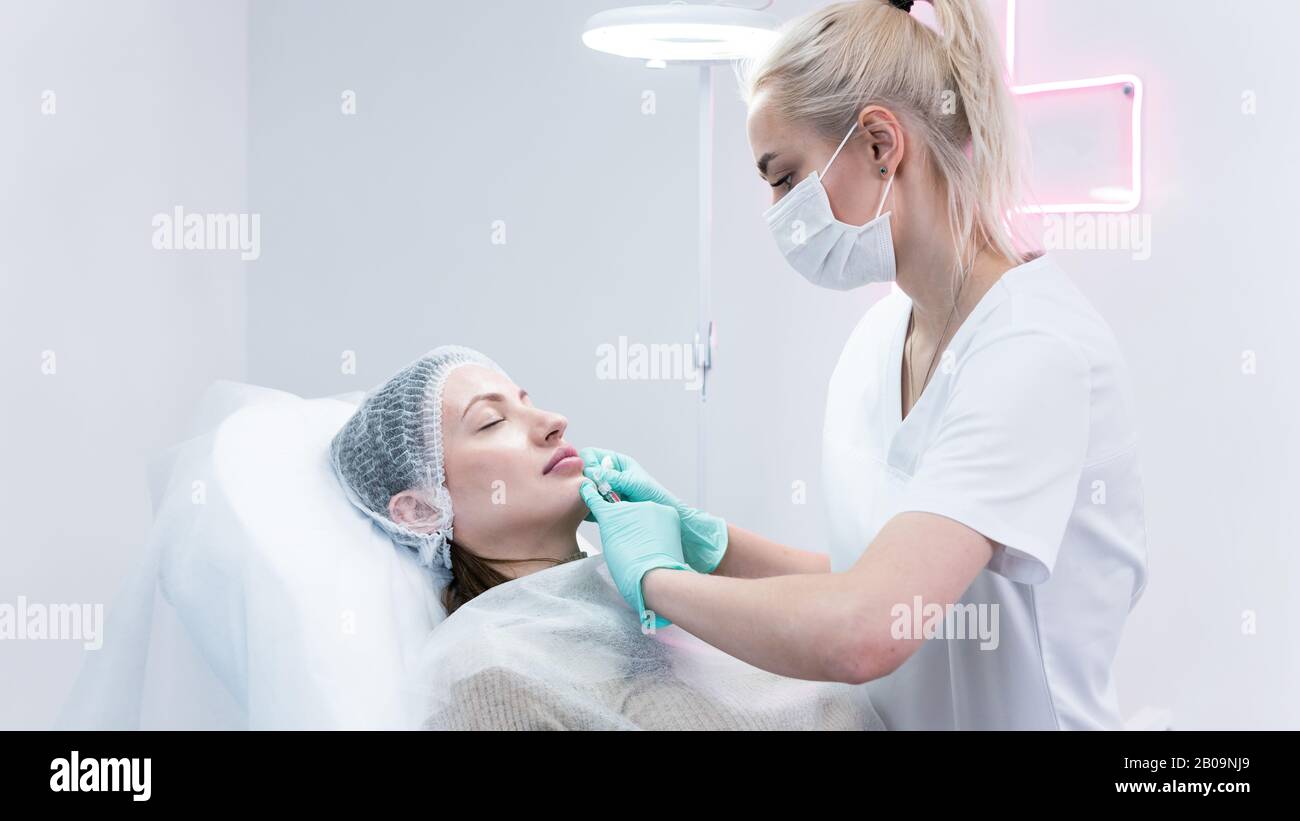 The young beautician doctor preparing to making injection in female lips. The doctor cosmetologist makes lip augmentation procedure. Concept of beauty Stock Photo