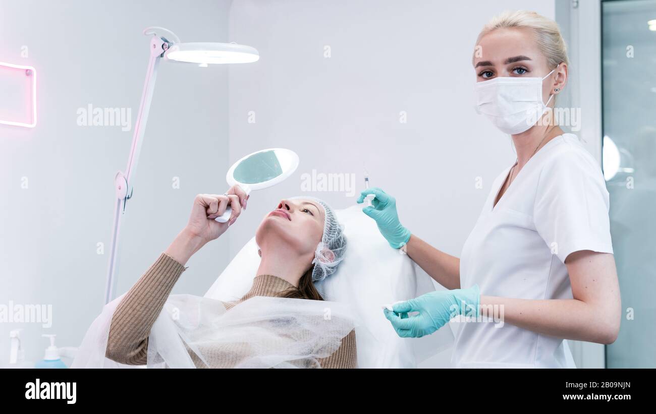 The young beautician doctor preparing to making injection in female lips. The doctor cosmetologist makes lip augmentation procedure. Concept of beauty Stock Photo