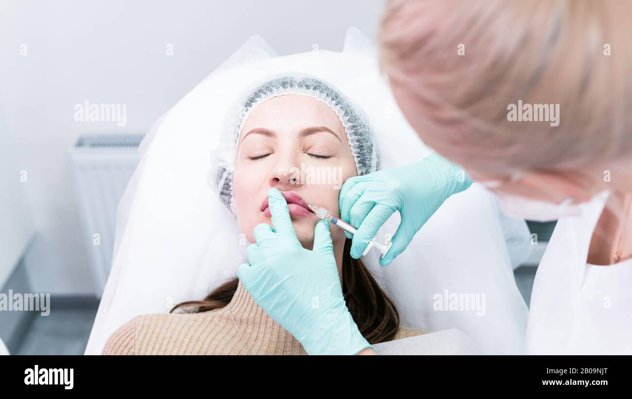 The young beautician doctor preparing to making injection in female lips. The doctor cosmetologist makes lip augmentation procedure. Concept of beauty Stock Photo