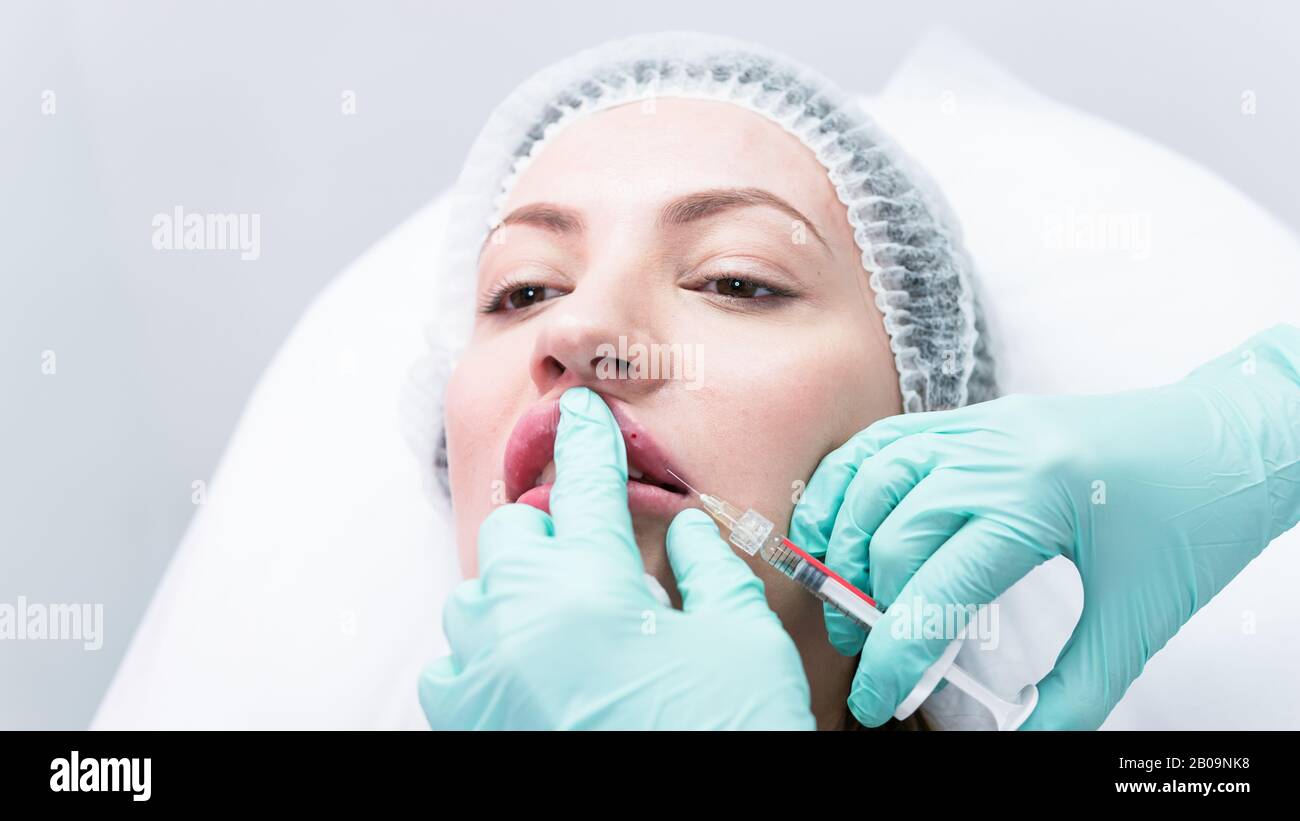 The young beautician doctor preparing to making injection in female lips. The doctor cosmetologist makes lip augmentation procedure. Concept of beauty Stock Photo