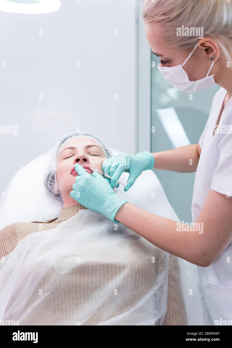 The young beautician doctor preparing to making injection in female lips. The doctor cosmetologist makes lip augmentation procedure. Concept of beauty Stock Photo