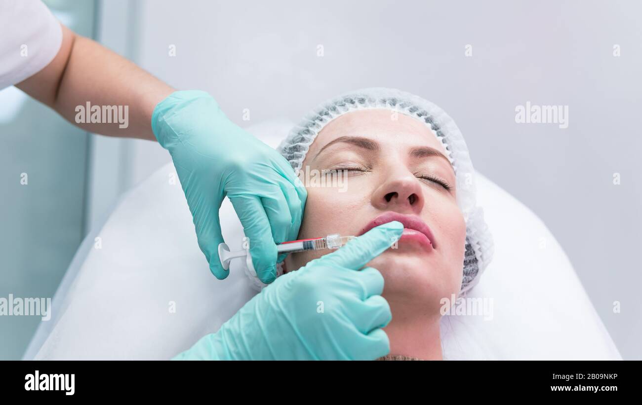 The young beautician doctor preparing to making injection in female lips. The doctor cosmetologist makes lip augmentation procedure. Concept of beauty Stock Photo