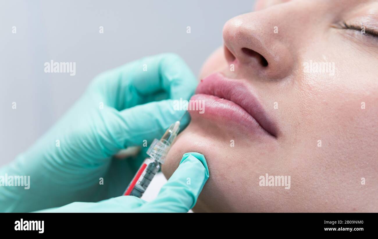 The young beautician doctor preparing to making injection in female lips. The doctor cosmetologist makes lip augmentation procedure. Concept of beauty Stock Photo
